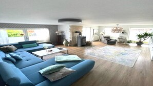 Una sala de estar moderna con un sofá azul, una mesa de centro y una alfombra. Hay una chimenea, un comedor y vistas al exterior.