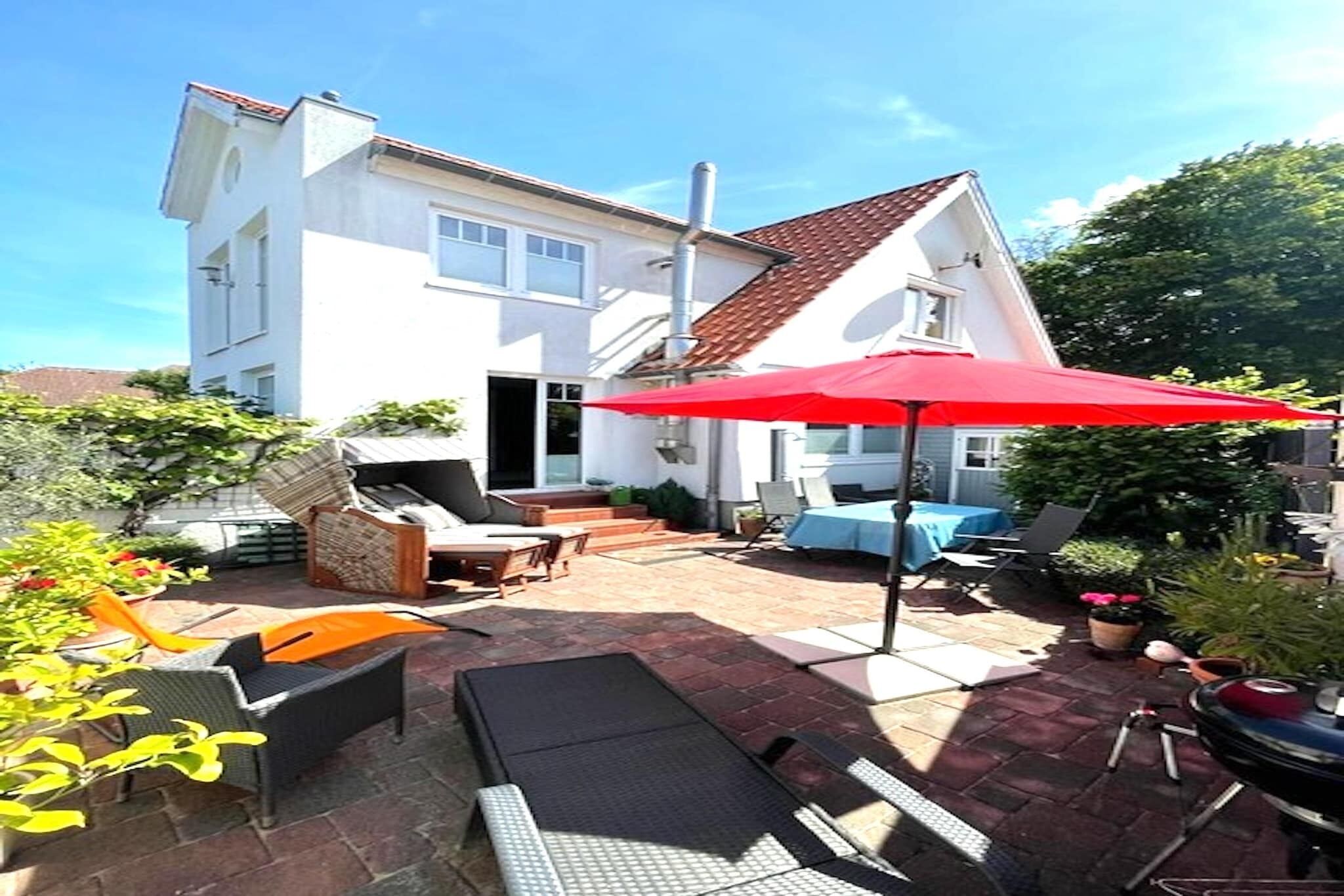 Une maison blanche avec un toit rouge, une terrasse avec des meubles d’extérieur et un parasol rouge.