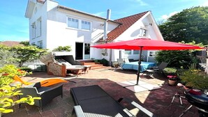 Una casa blanca con techo rojo, un patio con mobiliario exterior y un paraguas rojo.