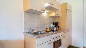 A compact kitchen with white cabinets, a stainless steel sink, a coffee machine, and a microwave.