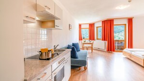 A compact kitchen with modern appliances, a dining area with a table and chairs, and a cozy seating area with a sofa and a bed.