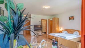 A hotel room with a bed, a TV, a wooden wardrobe, and a dining table with fruit and a vase.