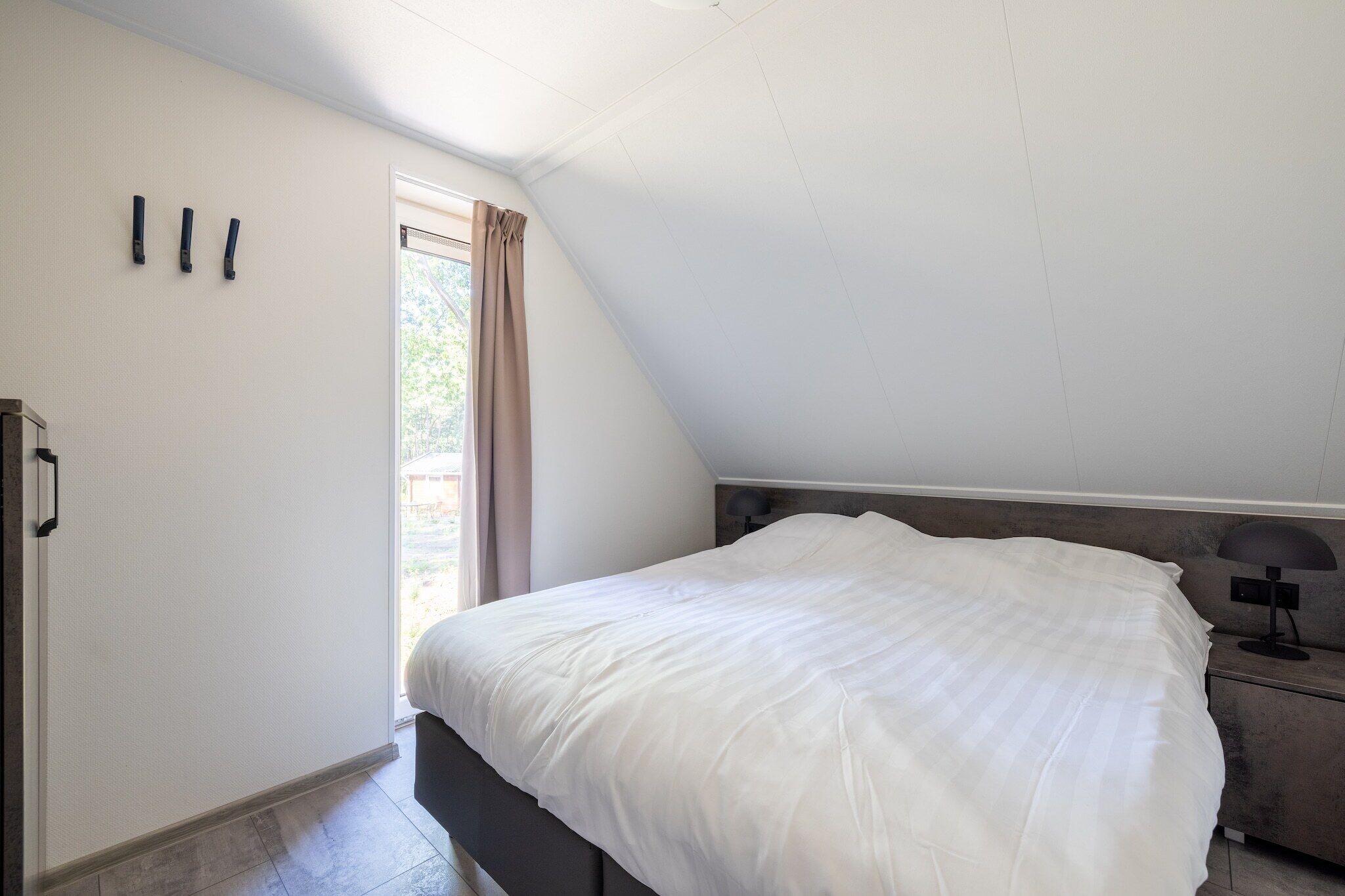 Une chambre à coucher avec un lit, une table de chevet, une lampe et une fenêtre avec des rideaux.