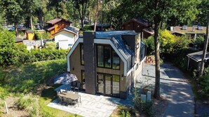 Et moderne hus med en stor glasdør, en terrasse med udendørs møbler og en omkransende have.