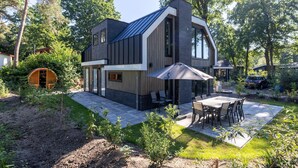 Et moderne hus med en stor terrasse, spiseplads og en træfad.
