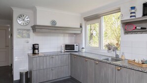 Une cuisine moderne avec des meubles gris, un four à micro-ondes, une machine à café et une fenêtre donnant sur un paysage verdoyant.