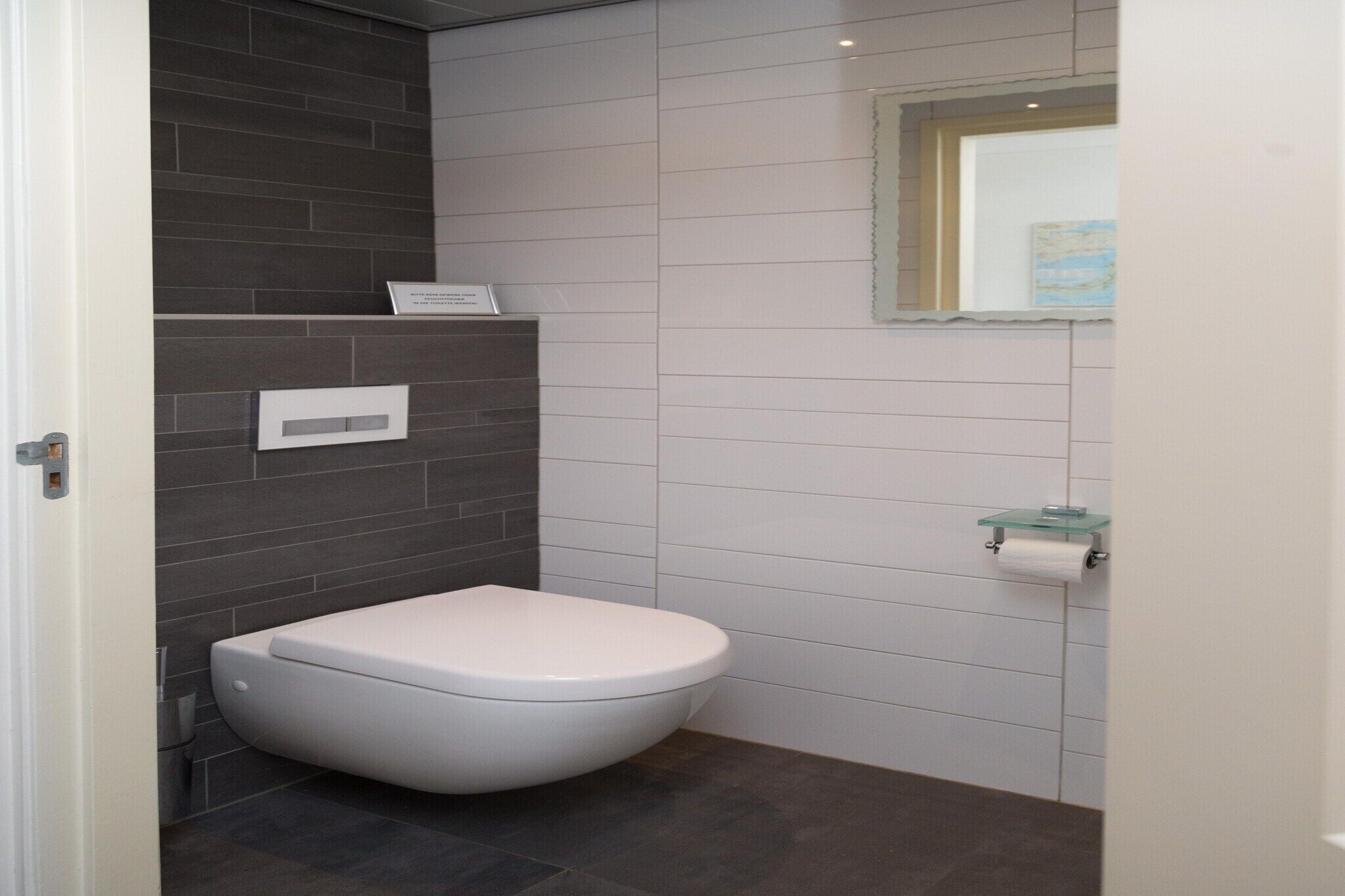 Une salle de bain moderne avec des toilettes blanches, des murs recouverts de carreaux foncés et un porte-savon en verre.