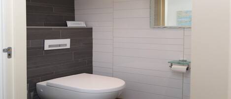 Une salle de bain moderne avec des toilettes blanches, des murs recouverts de carreaux foncés et un porte-savon en verre.