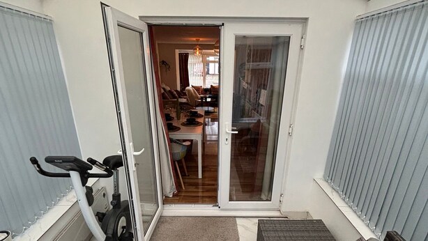 Un espacio habitable compacto con una puerta corredera de vidrio que da a un comedor, una bicicleta estática y una zona de estar con un otoman gris.