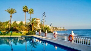 Ein Schwimmbad mit Blick auf den Ozean, Palmen und einem Gebäude im Hintergrund.