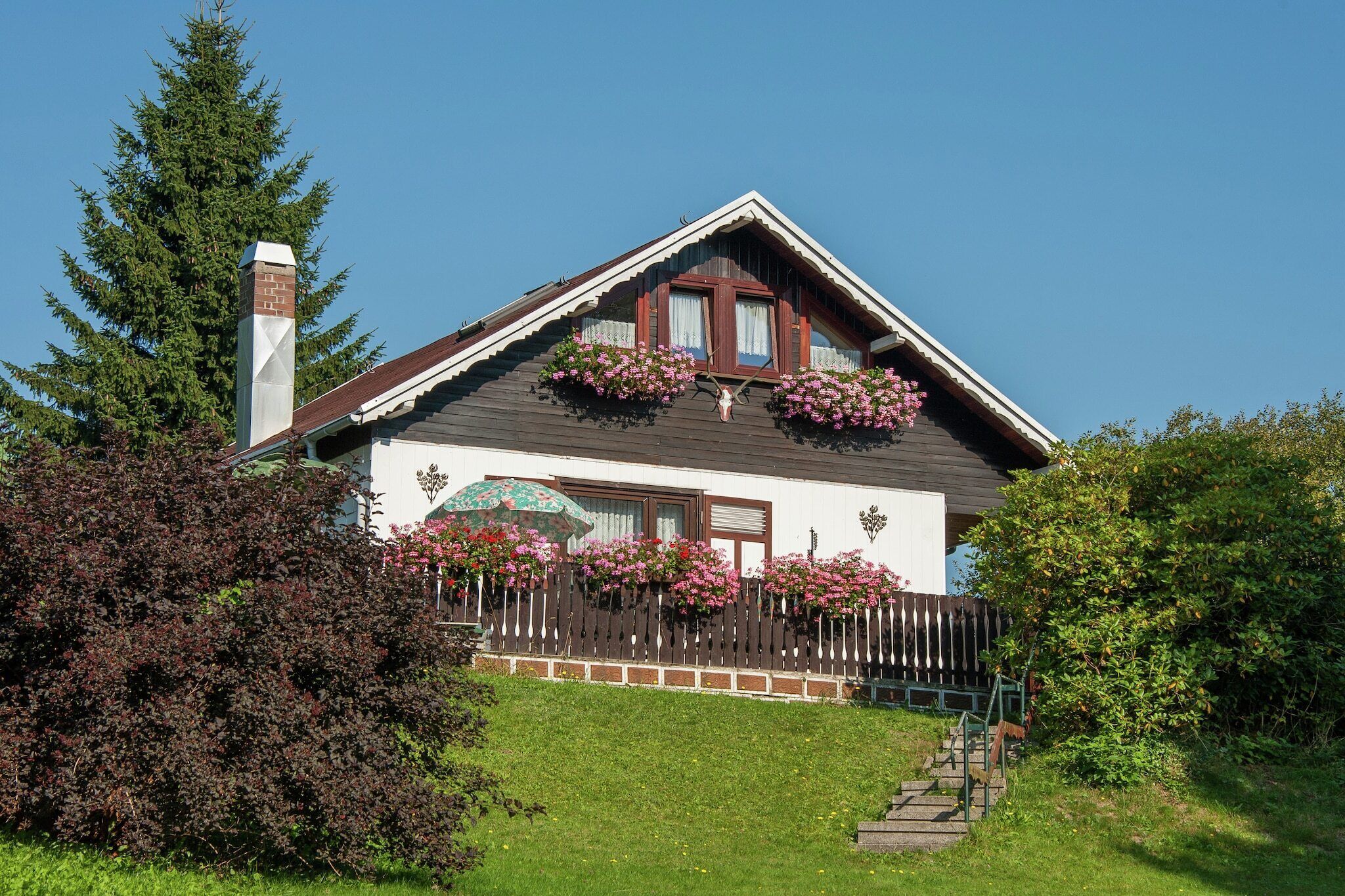 A house with a sloped roof, a brick chimney, and a wooden fence.