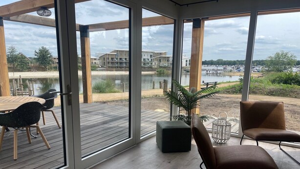 Une pièce moderne avec de grandes fenêtres, une terrasse en bois, une table avec des chaises et une plante en pot.