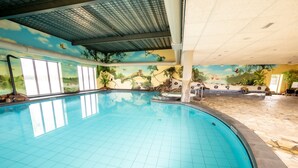 Une piscine intérieure aux murs et au plafond recouverts de carreaux, ornée de fresques représentant des paysages tropicaux et des animaux sauvages.