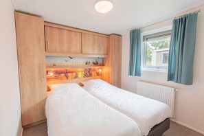 Ein Schlafzimmer mit einem Bett, Holzschränken, einem Fenster mit Vorhängen und einer Heizung.