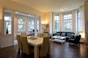 Relax in this stylish living room with a large dining table, comfortable sofa, and expansive windows offering views of the outdoors.