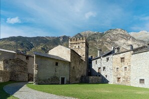 A historic stone building with a tower, surrounded by a cobblestone path and grassy areas, set against a mountainous backdrop. - Stone House near Cerler Ski Resort (Benasque)