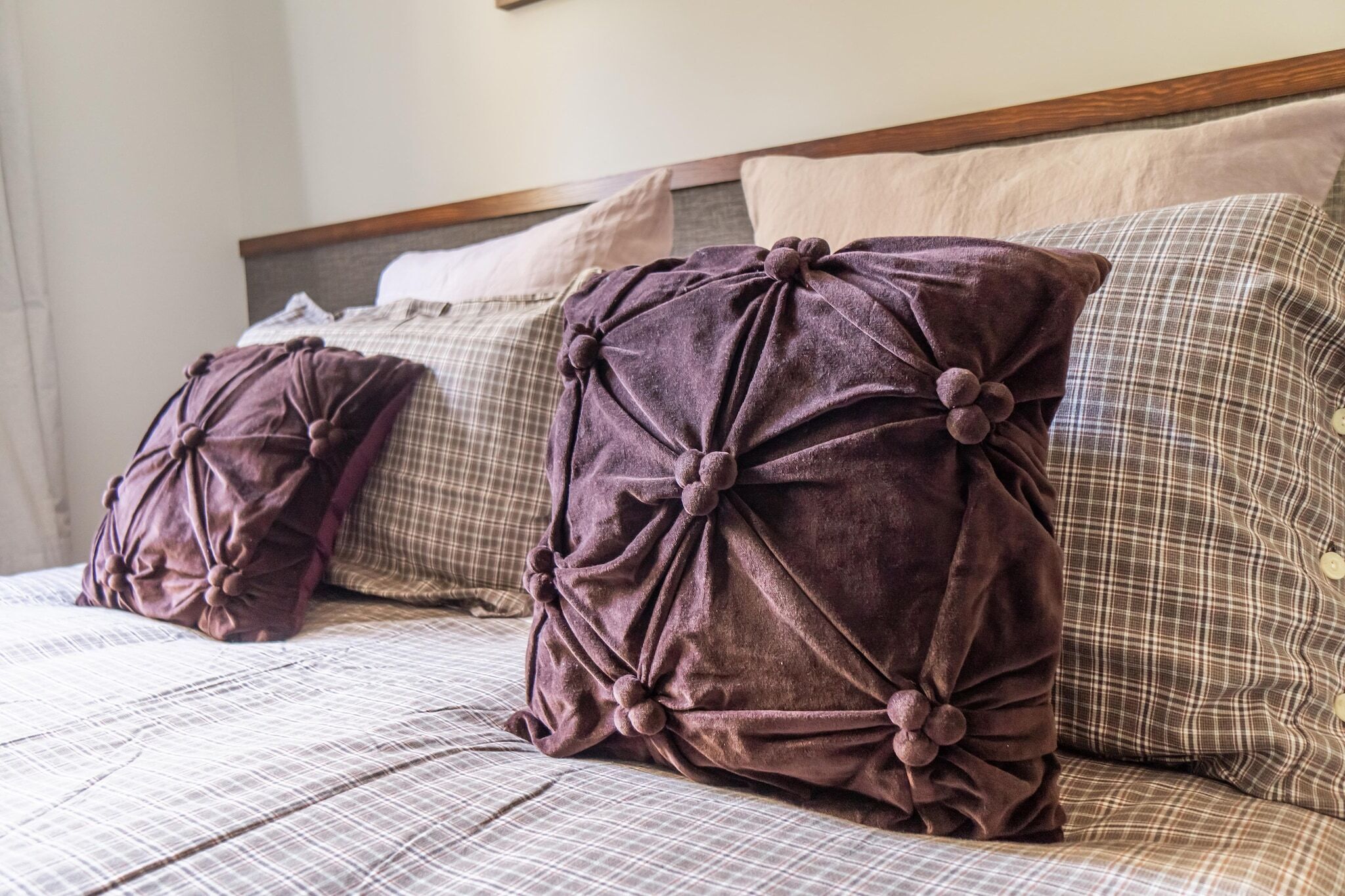 Uma cama com colcha xadrez e várias almofadas, incluindo duas almofadas roxas grandes e com nós.