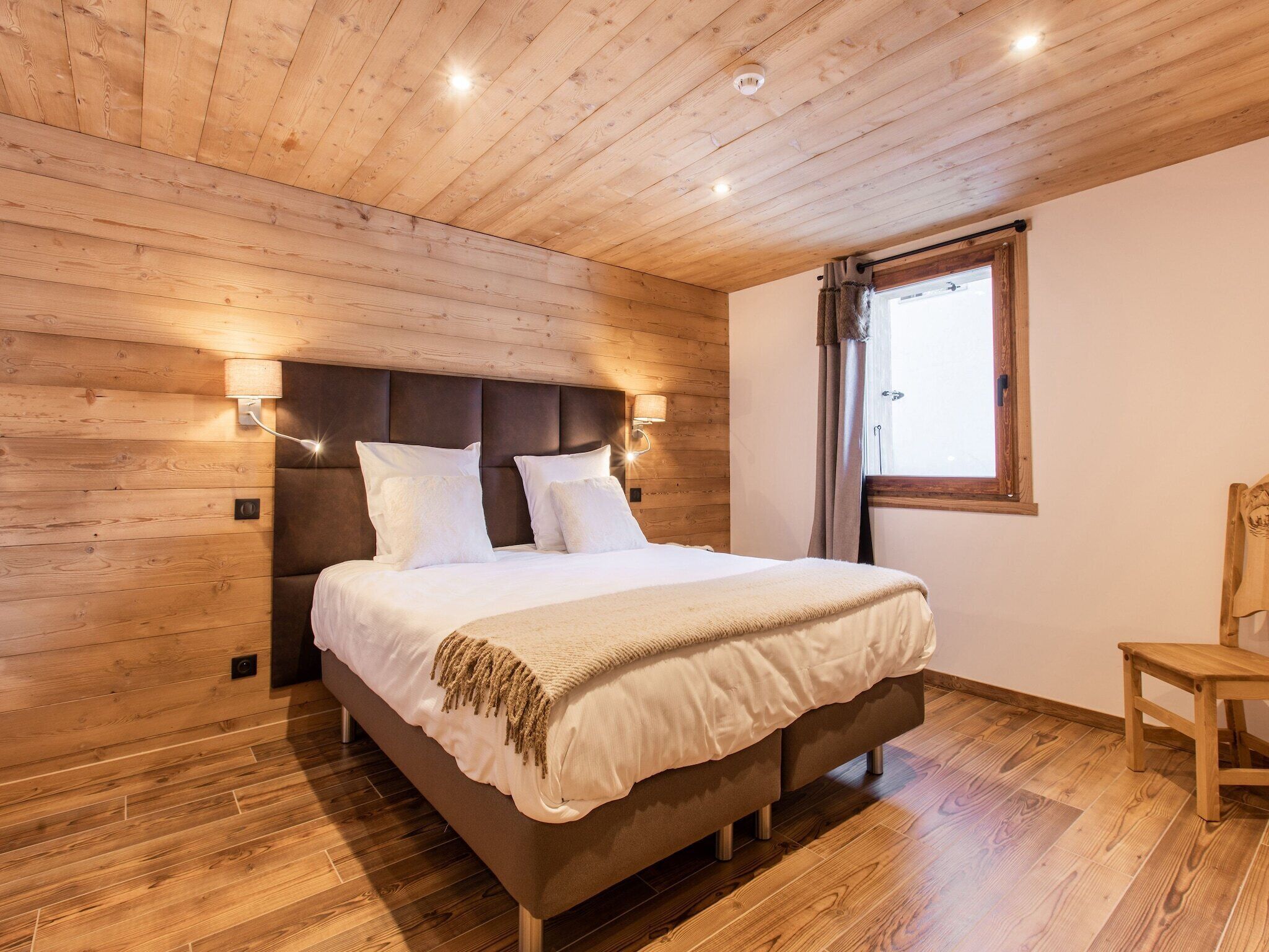 A bedroom with a wooden ceiling, a bed with white bedding, two bedside lamps, and a window with curtains.