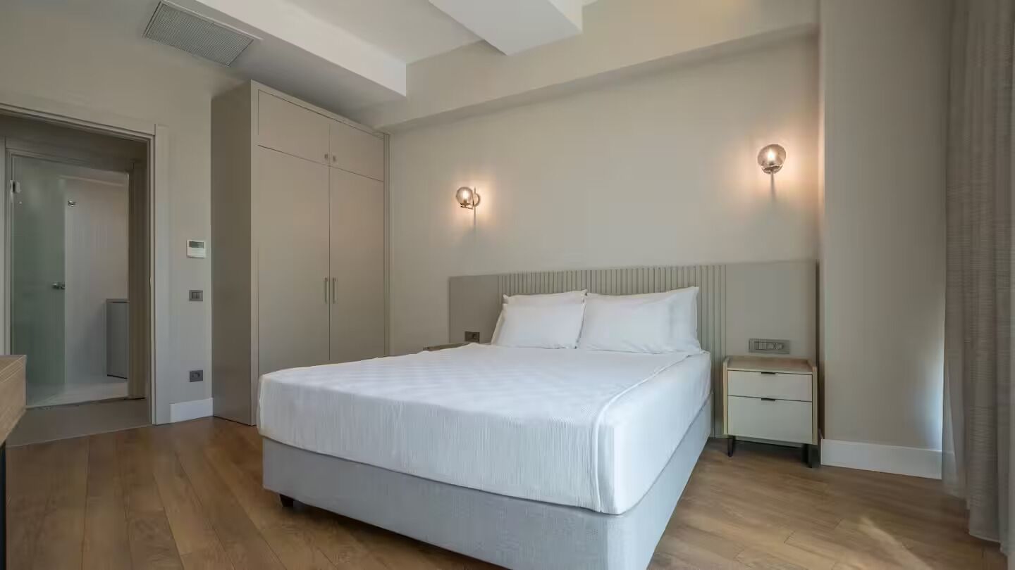A bedroom with a large bed, a nightstand, a wardrobe, and two wall-mounted lights.