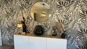 A white console table with a round mirror above it, set against a wall with a tropical leaf pattern wallpaper. - Modern house in Jalhay with terrace (Jalhay)