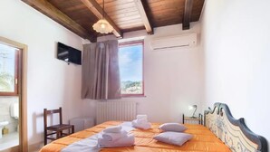 A bedroom with a wooden ceiling, a bed with an orange bedspread, a television on the wall, and a window with curtains.