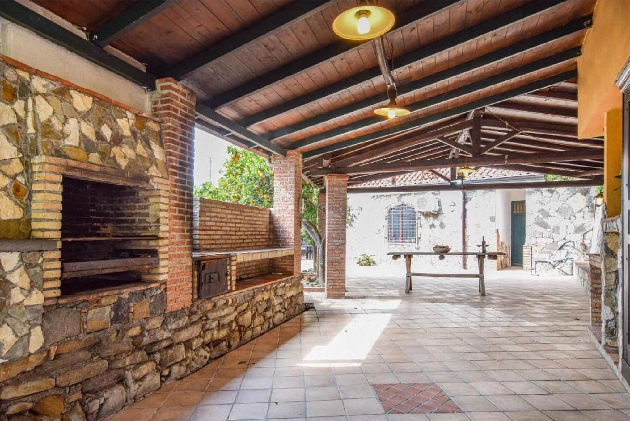 Eine Terrasse im Freien mit Kamin aus Stein, Holzbalken und gefliestem Boden.