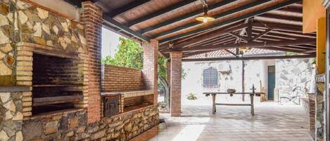 An outdoor patio with a stone fireplace, wooden beams, and a tiled floor.