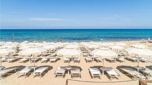 A beach with rows of sunbeds and umbrellas, a clear blue sky, and the sea in the background.