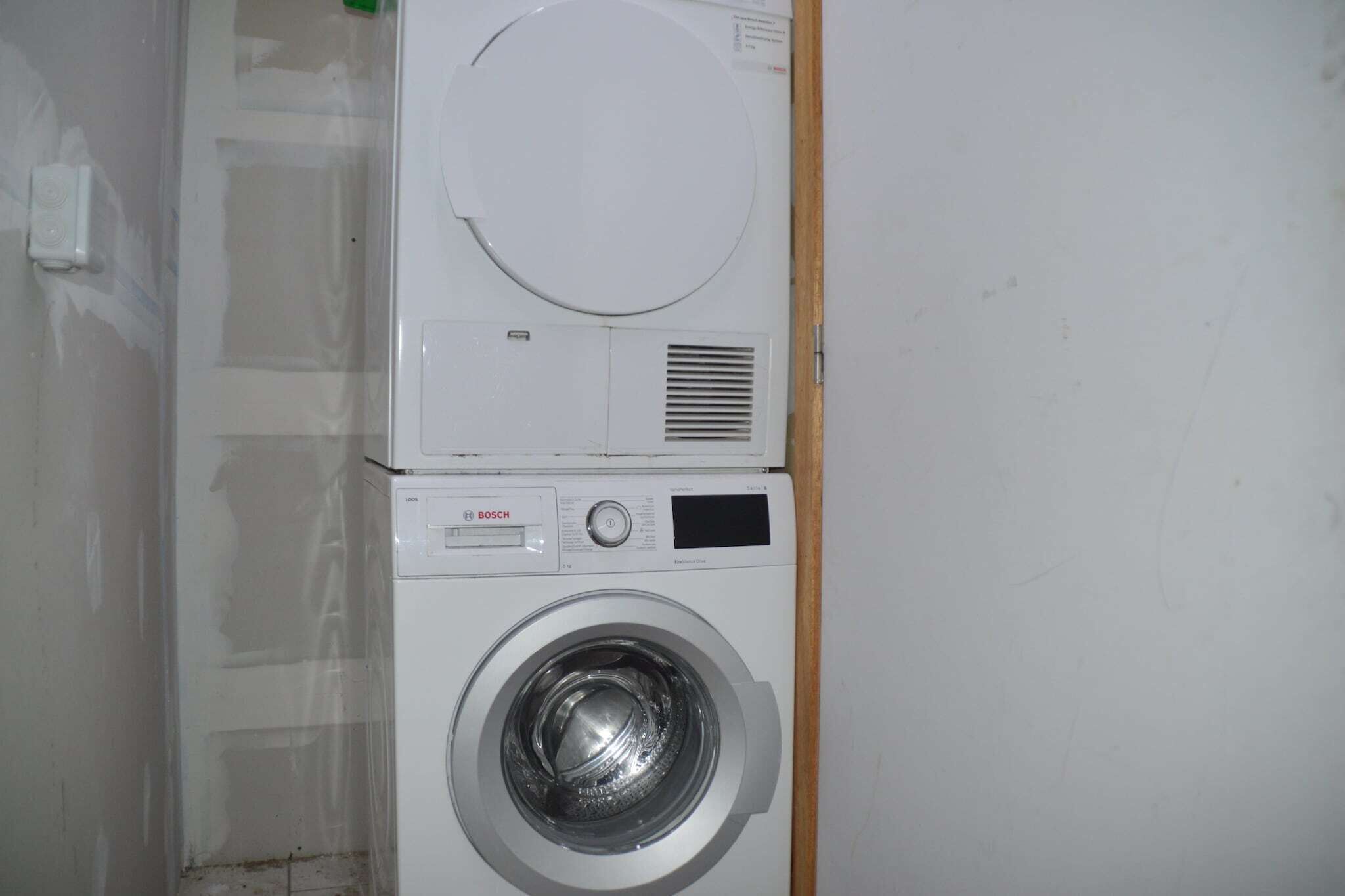 A stacked washer and dryer unit in a room with plain walls and a wooden door frame.