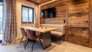 A modern dining area with a wooden ceiling, a TV mounted on the wall, and a window with curtains. - Apartment with shared infinity pool (St. Martin am Tennengebirge)