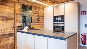 A modern kitchen with wooden accents, a large island with a sink, and built-in appliances. - Apartment with shared infinity pool (St. Martin am Tennengebirge)