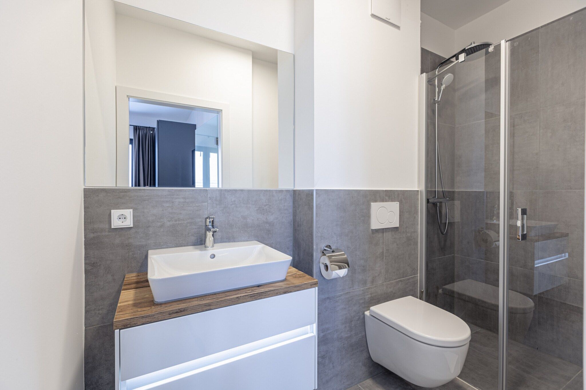 Ein modernes Badezimmer mit großem Spiegel, Waschbecken in Weiß, Toilette und einer Duschkabine.