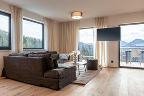 A modern living room with a sectional sofa, a flat-screen TV, and a balcony with a view of the mountains. - Apartment with shared infinity pool (St. Martin am Tennengebirge)