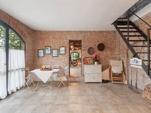 Una stanza rustica con pareti in mattoni a vista, un'area pranzo con tavolo e sedie, un armadietto bianco e una scala.