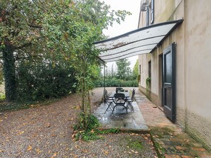Una veranda esterna con tavolo e sedie, una zona coperta e un edificio con porta e finestra.