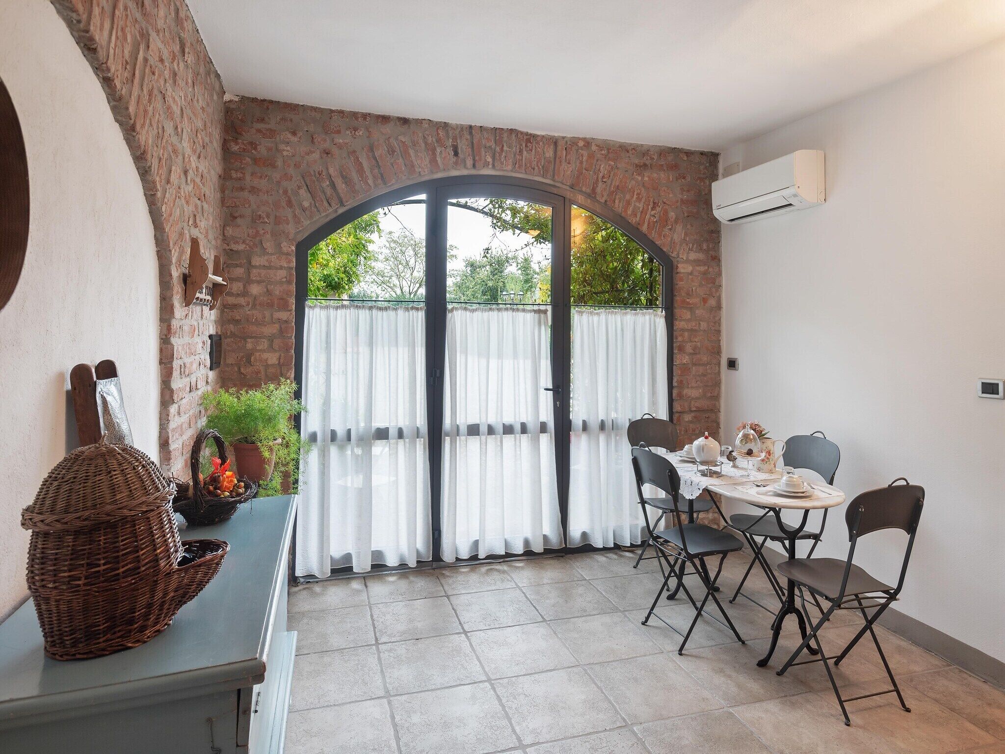Un coin repas avec un mur en briques, une grande fenêtre avec des rideaux et une table dressée pour deux personnes.
