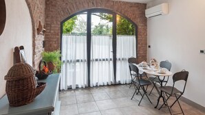 Un comedor con pared de ladrillo, un ventanal con cortinas y una mesa preparada para dos.