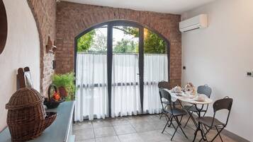 Un coin repas avec un mur en briques, une grande fenêtre avec des rideaux et une table dressée pour deux personnes.