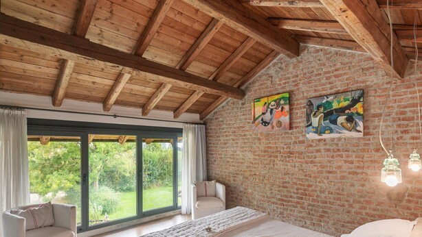 Un dormitorio con una ventana grande, una cama, una silla y una pared de ladrillo.