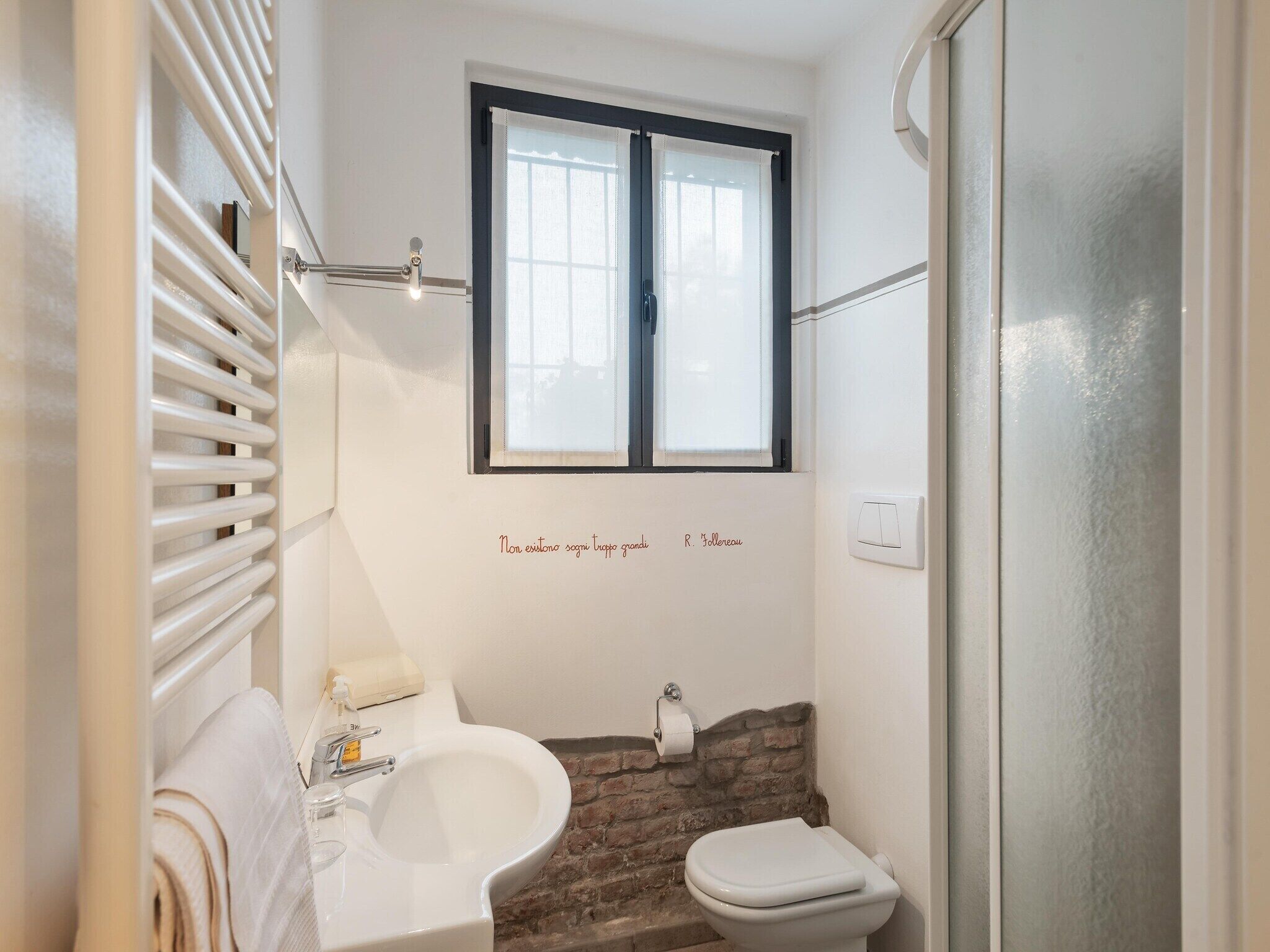 A compact bathroom with a white sink, a toilet, and a window above the sink.