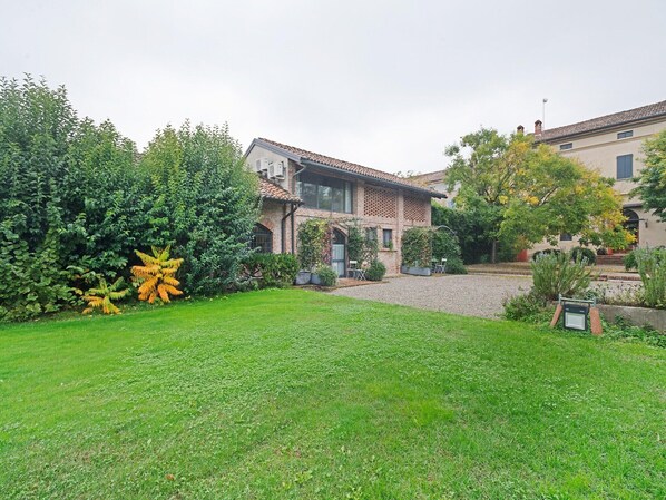 Un immobile residenziale con un prato ben curato, una casa in mattoni con tetto in tegole e un giardino ricco di piante e arbusti.