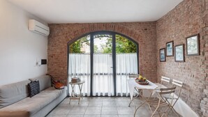 Una habitación acogedora con pared de ladrillo, un sofá, una mesa de comedor con sillas y un ventanal con cortinas.