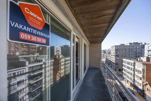 A balcony with a view of a cityscape, a Caenen sign, and a contact number.