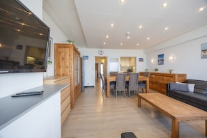 A modern living room with a wooden dining table, a sofa, and a TV on a stand.