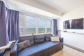 A modern living room with a large window, a flat-screen TV, and a leather sofa.