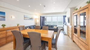 Una sala de estar moderna con una mesa de comedor de madera, asientos cómodos, un sofá y un amplio ventanal con vistas.