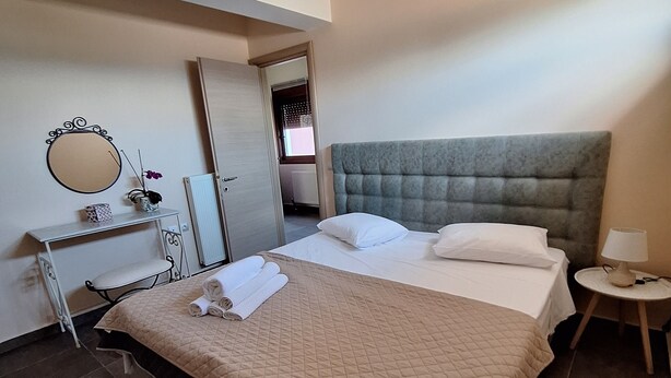 A neatly arranged bedroom with a bed, bedside table, lamp, and a mirror. - Naiad Studio Sea View (Poros)