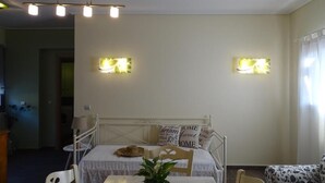 A bedroom with a bed, bedside table, and a potted plant. There are two wall-mounted lights and a window with curtains. - Naiad Studio Sea View (Poros)
