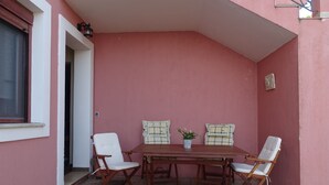A small patio with a wooden table and four white folding chairs. - Naiad Studio Sea View (Poros)