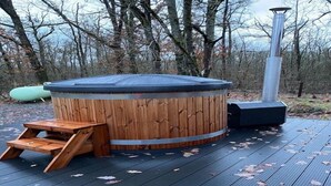 Un bain à remous en bois, doté d’une cheminée en métal, d’un banc en bois et d’une terrasse parsemée de feuilles.